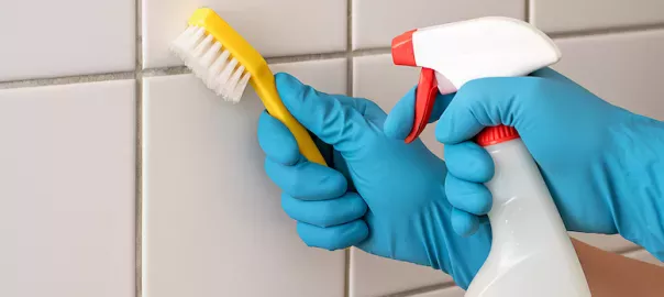 "Person rengör kakelfogar med borste och rengöringsmedel – jämförelse mellan naturliga metoder som bikarbonat och kemiska produkter för rena fogar i badrum och kök"